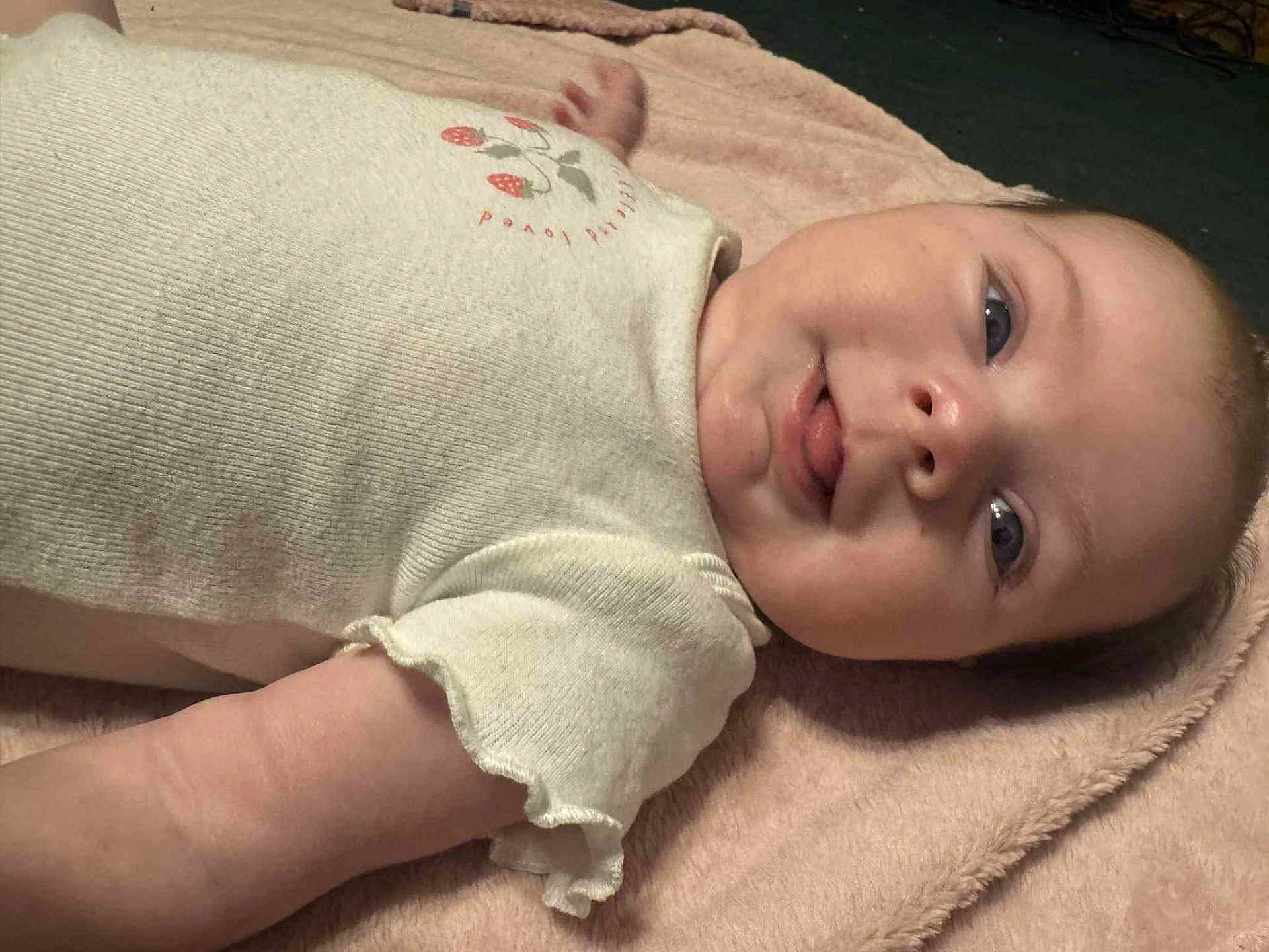 Haisley joined the competition — help win amazing prizes! baby, infant, face, tongue, clothing, onesie, blanket, lying_down, cute, child, soft_texture, pink, cream_color, playful, skin, head, arm, sleepwear, young_child, portrait