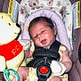 baby, infant, car_seat, plush_toy, winnie_the_pooh, yellow_outfit, mittens, baby_toy, child, seat_belt, safety_harness, floral_pattern, cute, indoors, smiling, foot, head, face, person, soft_toy