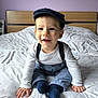 Maëlio participe au concours pour gagner de l'argent avec cette photo : baby, bed, blanket, blue_pants, blue_socks, cap, child, cute, face, happy, headwear, home, indoor, person, portrait, sitting, smiling, suspenders, toddler, white_shirt