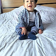 Maëlio participe au concours pour gagner de l'argent avec cette photo : baby, bed, blanket, child, clothing, happy, hat, headboard, home, indoor, pants, person, portrait, purple_wall, shirt, sitting, smiling, socks, toddler, young_child