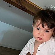 Tony participe au concours pour gagner de l'argent avec cette photo : baby, child, toddler, face, person, indoor, white_clothing, wooden_beam, curious_expression, buttoned_shirt, skin, head, hair, holding, wall, floor, portrait, casual, young, looking