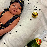 Kyrie is registered to the contest to win money with this photo: baby, black_and_gold, celebration, close_up, confetti, cute, festive, gold_ornament, hat, infant, lying_down, milestone, newborn, portrait, smiling, soft_texture, sparkling_juice, star_pattern, two_months, white_blanket