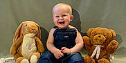 Thomas is registered to the contest to win money with this photo: baby, child, denim_overalls, smiling, happy, sitting, plush_bunny, teddy_bear, quilt, blanket, indoor, portrait, cute, barefoot, toy, soft_toy, green_background, infant, joyful, cuddly