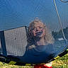 Hudson is registered to the contest to win money with this photo: child, smiling, trampoline, netting, mesh, outdoor, grass, blue_sky, sunlight, play, happy, person, red_shorts, recreation, leisure, daytime, fun, childhood, face, texture