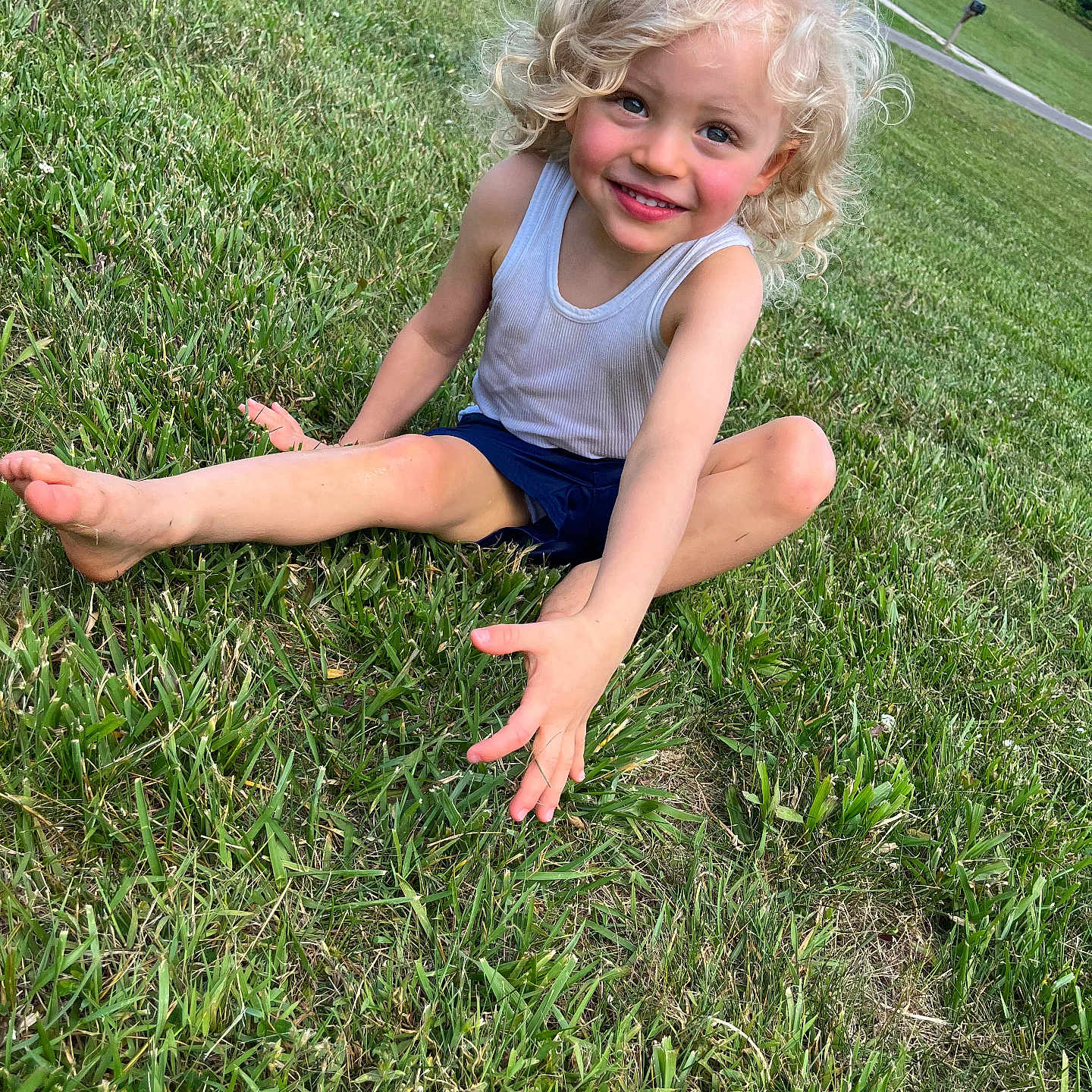 Hudson joined the competition — help win amazing prizes! child, curly_hair, smiling, grass, outdoor, summer, greenery, tank_top, shorts, barefoot, happy, playful, sitting, nature, daylight, person, young, park, casual, fun