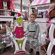 Liam is registered to the contest to win money with this photo: child, boy, smiling, indoor, holiday, christmas, grinch, cutout, decorations, candy, shop, flooring, clothing, sneakers, display, festive, toy, portrait, standing, happy