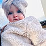 baby, child, face, blue_eyes, knit_hat, bow, fluffy_jacket, winter_clothing, outdoor, sky, portrait, cute, warm_clothing, infant, headwear, soft_texture, smile, person, close_up, daylight