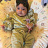 baby, infant, child, portrait, lying_down, smiling, wide_eyed, bow_headband, green_outfit, pacifier, baby_toy, stuffed_animal, patterned_blanket, baby_bouncer, indoor, close_up, adorable, relaxed, textile, family_photo
