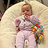 Kyara is registered to the contest to win money with this photo: baby, infant, child, portrait, lying_down, blanket, lavender_clothing, onesie, plush_toy, unicorn_toy, baby_toys, rattle, crib, nursery, indoor, face, wide_eyes, relaxed, colorful, soft_blanket