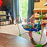 baby, child, indoor, activity_jumper, cat, carpet, television, curtains, window, furniture, toys, poster, cabinet, living_room, person, smiling, floor, blanket, sitting, home