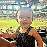 Addilyn is registered to the contest to win money with this photo: baby, child, stadium, baseball, headband, stars, celebration, person, happy, smiling, outdoor, daylight, spectator, clothing, earrings, hand, grass, people, sports, event