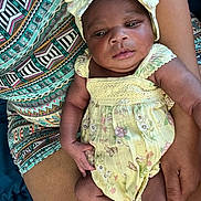 Makayla joined the competition — help win amazing prizes! baby, child, infant, yellow_dress, bow, floral_pattern, arm, hand, skin, person, lap, colorful_clothing, patterned_dress, resting, cute, newborn, portrait, indoors, soft_lighting, comfort