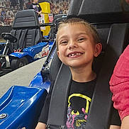 Wyatt is registered to the contest to win money with this photo: child, boy, smile, go_kart, seatbelt, racing, indoor, helmet_absent, background, girl, checkered_ceiling, mural, vehicle, seat, happy, fun, leisure, race_track, person, sport