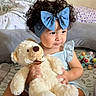 Amelia Guerrero joined the competition — help win amazing prizes! toddler, child, curly_hair, blue_bow, headband, teddy_bear, plush_toy, bed, bedding, toy, colorful, cute, indoor, person, smile, sitting, soft, cozy, playful, young_child