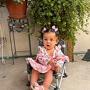 Amelia Guerrero is registered to the contest to win money with this photo: toddler, child, girl, pink_dress, sandals, hair_bows, chair, potted_plants, greenery, outdoor, curious, sitting, footwear, baby, cute, small_chair, floor, plant_stand, portrait, young_child