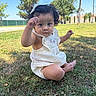 toddler, child, grass, outdoor, park, sunny, curly_hair, white_dress, baby, nature, greenery, trees, sitting, cute, person, young_child, daylight, playful, expression, barefoot