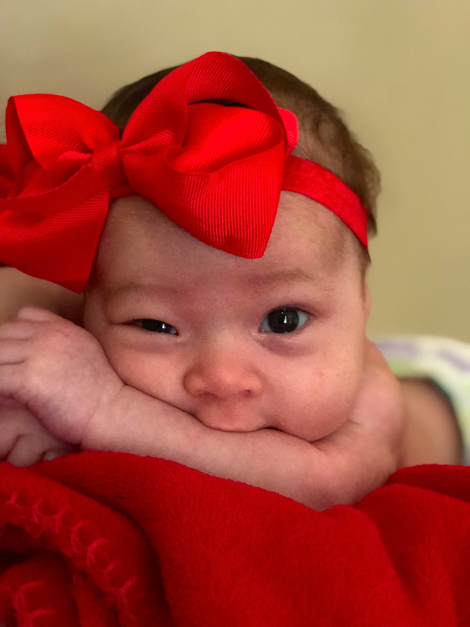 Mia is registered to the contest to win money with this photo: cheek, child, close_up, eye, eyebrow, face, finger, forehead, hair_accessory, head, headband, headgear, infant, lip, mouth, nose, person, red, skin, smile