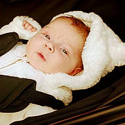 Thalia is registered to the contest to win money with this photo: baby, infant, face, hood, white_clothing, stroller, child, cute, soft_texture, portrait, young_child, fur, clothing, baby_boy, baby_girl, outdoor_gear, warm_clothing, baby_carrier, seatbelt, resting