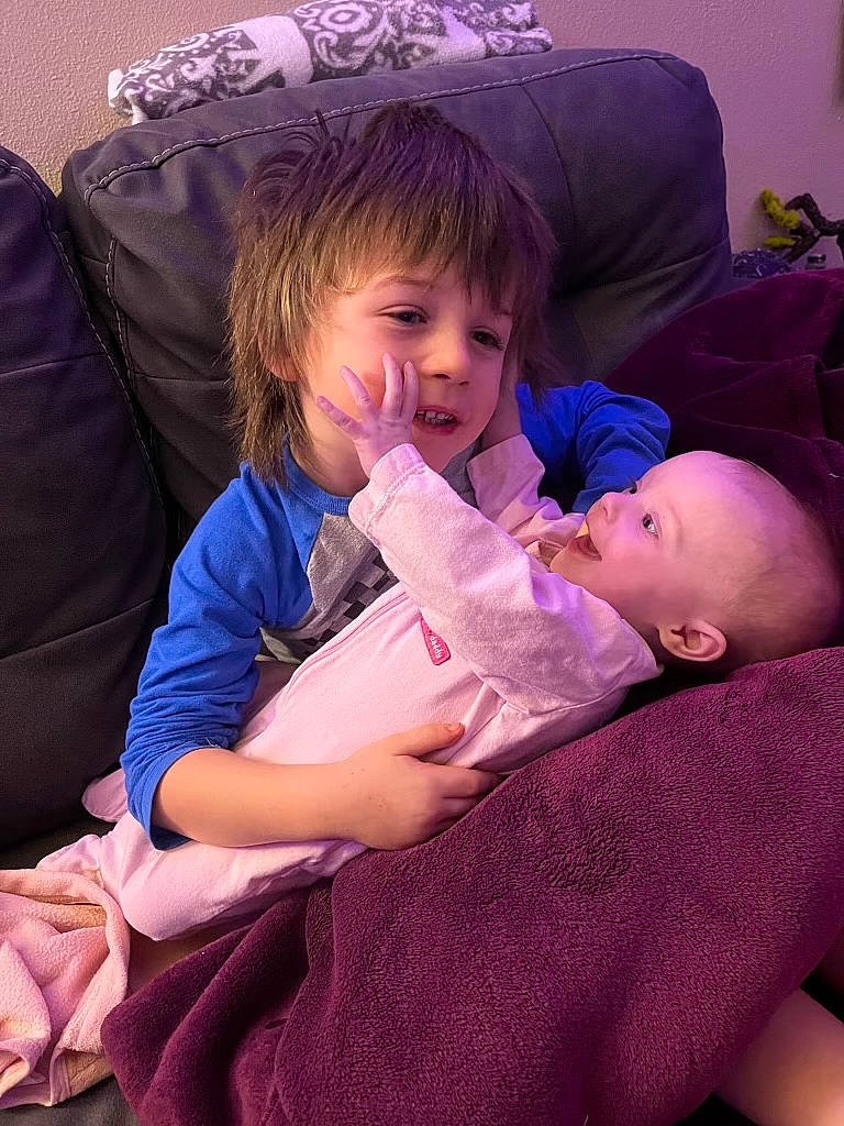 Juniper is registered to the contest to win money with this photo: baby, baby_toddler_clothing, cheek, comfort, ear, eye, face, facial_expression, finger, hairstyle, human, human_body, iris, lap, mouth, person, product, purple, skin, toddler