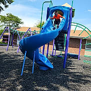 Jeremiah Bates is registered to the contest to win money with this photo: child, playground, slide, sliding, outdoor, sunny, blue_slide, orange_shirt, playground_equipment, climbing_bars, swings, trees, sky, clouds, brick_building, rubber_mulch, recreation, summer, portrait, fun