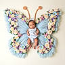 Kaiyah is registered to the contest to win money with this photo: baby, infant, butterfly_wings, flowers, pastel_colors, tulle, knitted_antennae, costume, cute, portrait, floral_arrangement, blue, pink, purple, white, green_leaves, soft_texture, adorable, child, whimsical