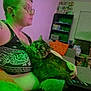 black_tank_top, cat, cat_tree, couch, glasses, green_light, home, indoor, living_room, orange_pillow, person, pet, pillow, relaxed, remote_control, shelf, short_hair, tattoo, tattooed_arm, window