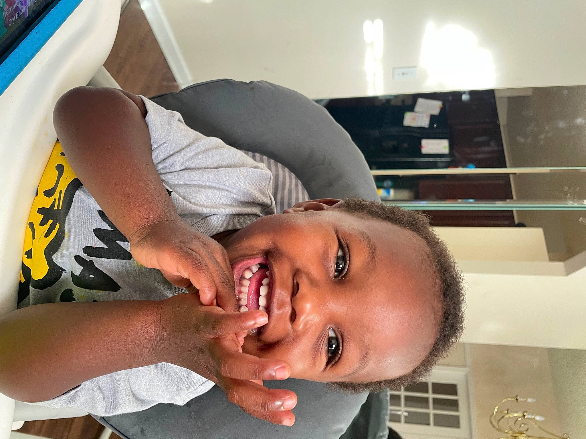 Malachi is registered to the contest to win money with this photo: arm, chest, child, comfort, elbow, eyelash, eyewear, forehead, fun, gesture, happy, human_leg, jaw, joy, mouth, neck, person, shelf, smile, t_shirt