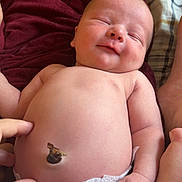 Tucker is registered to the contest to win money with this photo: baby, newborn, infant, diaper, umbilical_cord_stump, belly, belly_button, hand, fingers, smiling, sleeping, torso, skin, blanket, sheet, plaid_bed, maroon_blanket, portrait, closeup, parent_hand