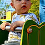 toddler, child, playground, outdoor, daylight, metal_bar, green, shirt, animal_print, giraffe, lion, curious, hands, clothing, park, person, short_hair, casual, seat, nature