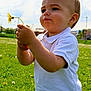toddler, child, dandelion, flower, grass, outdoor, nature, greenery, field, white_shirt, portrait, daylight, cute, young_child, summer, holding, serious_expression, baby, person, casual_clothing