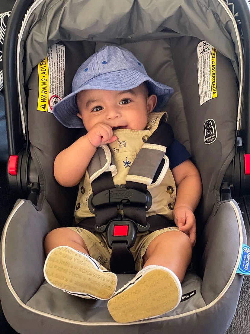 Gael is registered to the contest to win money with this photo: arm, auto_part, baby, baby_carriage, baby_in_car_seat, baby_products, baby_safety, car_seat, child, comfort, headwear, knee, motor_vehicle, person, personal_protective_equipment, photograph, sitting, thigh, tire, toddler