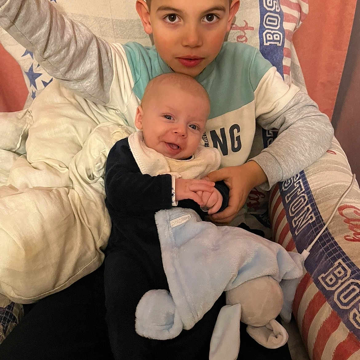 Ayden Harrault participe au concours pour gagner de l'argent avec cette photo : baby, blanket, boy, brother, child, clothing, couch, cozy, eyes, face, hands, holding, home_interior, patterned_fabric, pillow, plush_toy, portrait, seated, sibling, smile