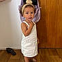 Alma a rejoint le concours — aidez-le/la à gagner de superbes lots ! toddler, child, white_dress, headband, curly_hair, sandal, wooden_floor, backpack, black_bag, door, indoor, standing, looking, hand_gesture, floor, footwear, person, young_child, casual_clothing, light_skin