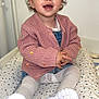Alma participe au concours pour gagner de l'argent avec cette photo : toddler, child, smiling, pink_sweater, white_sneakers, knitted_clothing, indoor, cushion, patterned_bedding, happy, cute, seated, young_child, clothing, portrait, person, feet, face, head, hands