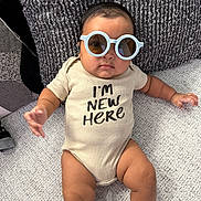 Noah joined the competition — help win amazing prizes! baby, sunglasses, onesie, couch, cushion, infant, child, text_on_clothing, indoor, relaxing, portrait, person, comfortable, fashion, cute, skin, plush, seated, expressionless, home