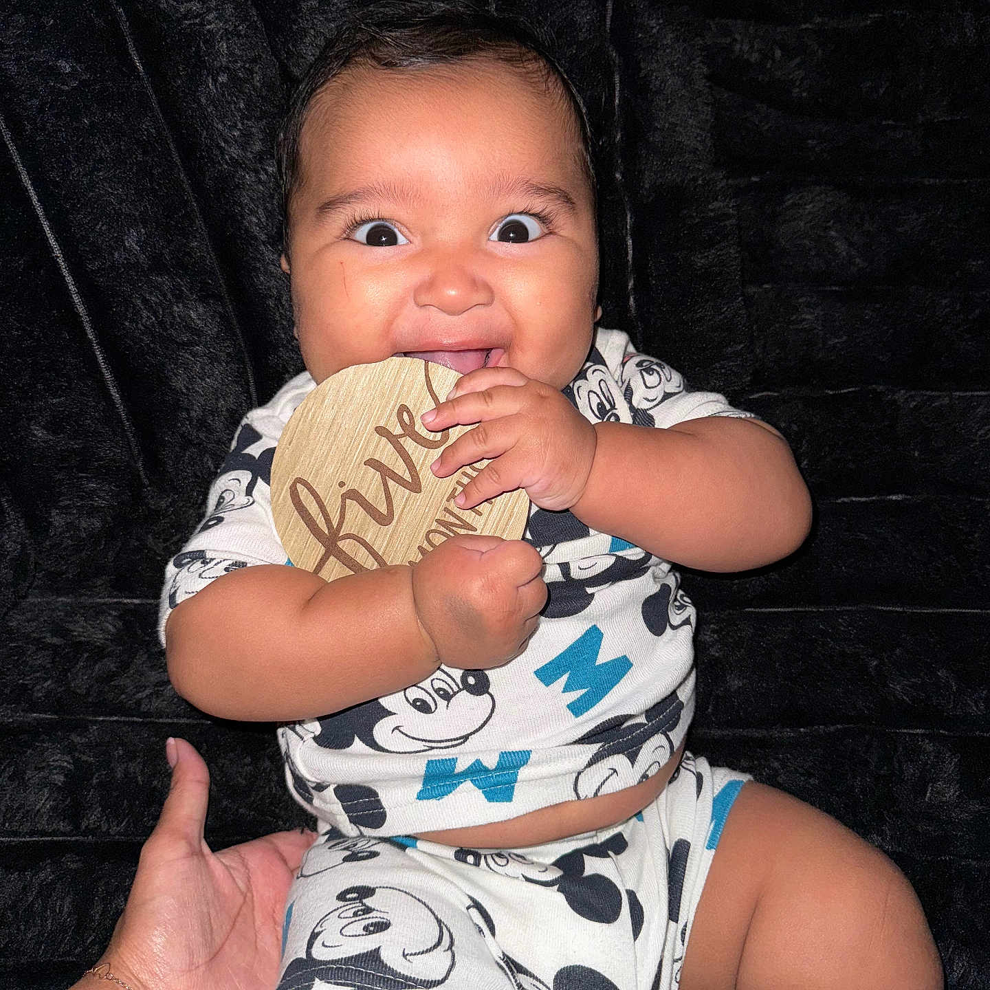 Noah joined the competition — help win amazing prizes! baby, black_background, child, chubby_cheeks, clothing, cute, expression, hand, happy, holding, indoor, infant, mickey_mouse, milestone, pajamas, person, portrait, sitting, smiling, wooden_plaque