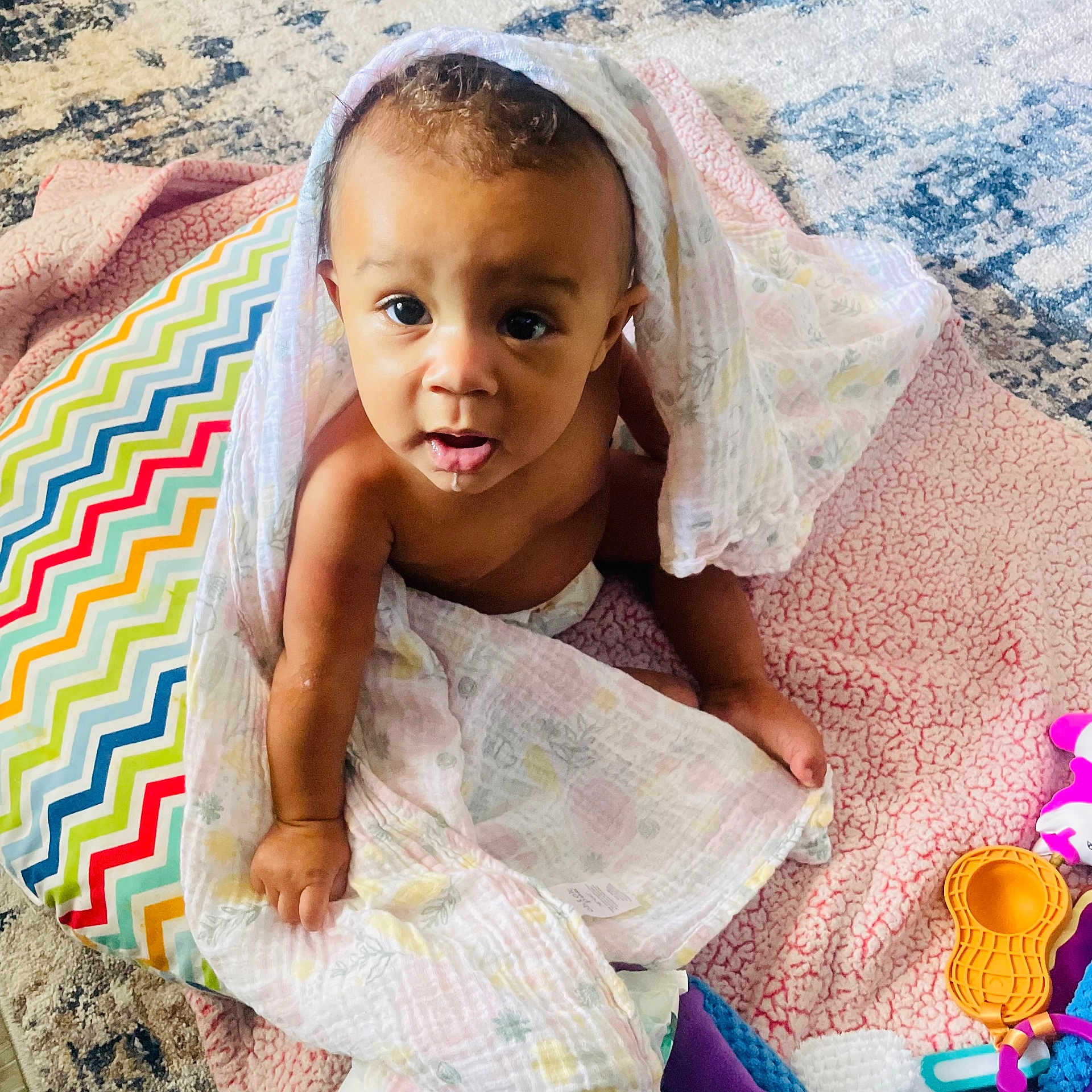 Ellie-Faye is registered to the contest to win money with this photo: baby, blanket, carpet, child, colorful, cushion, cute, drool, expression, floor, hand, head, indoor, infant, looking_up, pattern, person, sitting, skin, toy