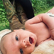 Waylon joined the competition — help win amazing prizes! baby, infant, face, skin, eyes, mouth, blanket, fur, cowboy_boots, hat, outdoor, nature, greenery, grass, portrait, closeup, resting, cute, expression, child