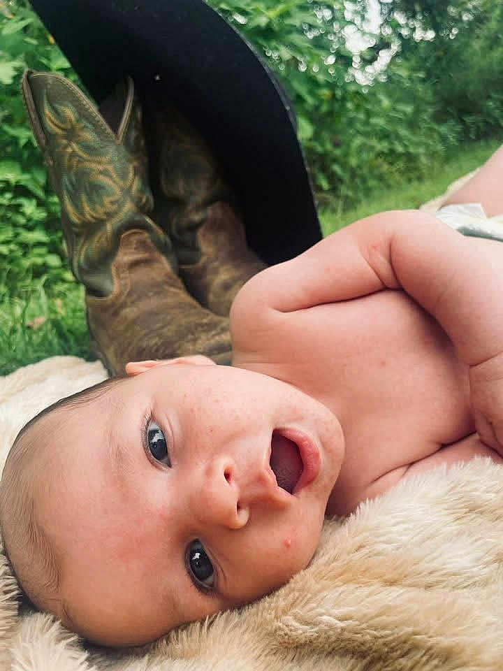 Waylon joined the competition — help win amazing prizes! baby, infant, face, skin, eyes, mouth, blanket, fur, cowboy_boots, hat, outdoor, nature, greenery, grass, portrait, closeup, resting, cute, expression, child