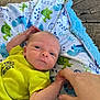 Isaiah is registered to the contest to win money with this photo: baby, newborn, infant, hand, finger, blanket, dinosaur_pattern, yellow_clothing, person, skin, face, eyes, lying_down, wooden_surface, cute, small, holding, child, toddler, soft