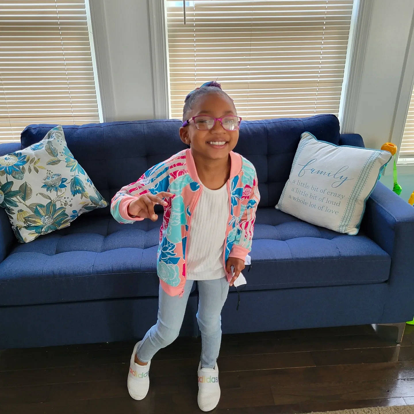 Anika is registered to the contest to win money with this photo: baby_toddler_clothing, comfort, couch, electric_blue, eyewear, flooring, furniture, happy, hardwood, joy, living_room, person, pillow, rectangle, sitting, sleeve, smile, sofa_bed, studio_couch, textile