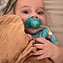baby, pacifier, blanket, bed, pillow, infant, hand, face, blue_clothing, indoor, child, cute, lying_down, soft_texture, skin, expression, comfort, rest, sleepwear, newborn