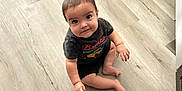 Ezekiel joined the competition — help win amazing prizes! child, toddler, floor, wooden_floor, indoor, sitting, curious, smiling, clothing, tshirt, shorts, person, young_child, face, barefoot, looking_up, home, cabinet, light, casual