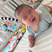 Ean is registered to the contest to win money with this photo: baby, smiling, tummy, toy, crib, colorful, happy, infant, clothing, playtime, child, indoors, cute, face, person, soft, blanket, striped, pattern, comfort