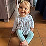 toddler, child, smiling, sitting, indoor, floor, tile, clothing, long_sleeve, pants, barefoot, face, hair, wooden_furniture, cabinet, hallway, bag, cute, happy, portrait