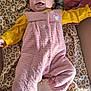 baby, child, onesie, pink_clothing, yellow_shirt, smile, tongue_out, leopard_print, blanket, soft_fabric, lying_down, happy, infant, face, person, indoor, cute, cozy, apparel, childrenswear