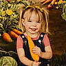 child, girl, pigtails, smiling, carrot, vegetables, garden, background, portrait, happy, overalls, pink_shirt, blonde_hair, nature, plants, produce, fresh, cute, outdoor, holding