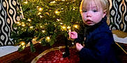Paige is registered to the contest to win money with this photo: baby, christmas, christmasdecorations, clothing, coat, couch, face, festival, fir, footwear, furniture, hardwood, head, lighting, person, photography, plant, portrait, tree, wood