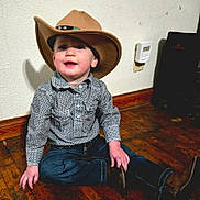 Charles joined the competition — help win amazing prizes! child, toddler, cowboy_hat, shirt, jeans, boots, floor, wooden_floor, indoor, sitting, smiling, curious, shadow, wall, plaid, patterned_clothing, young_child, cute, portrait, casual