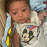 baby, infant, face, blanket, clothing, mickey_mouse, cartoon, expression, curious, wrapped, soft, cute, young_child, indoors, portrait, person, sleepwear, toddler, head, hand